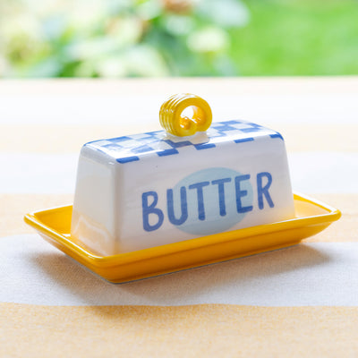 Butter dish with blue lid labeled 'BUTTER' on a yellow tray outdoors.